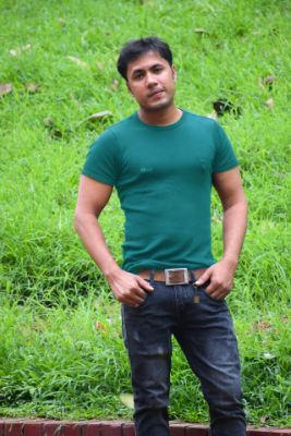 Young man wearing a green shirt. His hands are in his pockets and his expression is inviting.